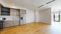 This single-floor unit showcases a contemporary design with clean lines and a neutral palette throughout. The open-concept main living area is anchored by light-toned hardwood flooring that extends seamlessly from the kitchen through the living space, creating a cohesive and airy feel. Recessed lighting and linear HVAC vents in the ceiling contribute to the modern aesthetic, while a ceiling fan adds comfort to the living area, which benefits from natural light through sliding glass doors that open to a private balcony.

The kitchen is efficiently designed with light wood-grain cabinetry, a stainless steel side-by-side refrigerator with water and ice dispenser, a stainless steel gas range, a microwave, and a marble-style tile backsplash. Open shelving adds a contemporary touch alongside ample upper and lower cabinet storage.

The bathroom is finished with large-format marble-look porcelain tile flooring, a soaking tub, a wood-grain vanity with a white countertop, and brushed metal fixtures. A spacious walk-in closet features marble-look tile flooring and metal hanging rods. A dedicated laundry room houses a full-size front-loading washer and dryer set with overhead shelving for added storage.