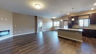 This single-floor residence offers a thoughtfully designed open-concept layout that seamlessly connects the living area and kitchen. Rich, dark hardwood-style flooring runs throughout the main living spaces, complemented by warm taupe walls and textured ceilings that lend a cozy yet polished ambiance. The spacious living area is bathed in natural light from multiple windows and opens directly to the kitchen, which is outfitted with dark espresso cabinetry, granite countertops, stainless steel appliances including a refrigerator, range, and microwave, and a central island with pendant lighting above. A door off the kitchen provides convenient exterior access. The bedrooms feature plush wall-to-wall carpeting and ample closet space, with windows allowing natural light to fill each room. The primary bathroom is equipped with a granite-topped vanity with dark wood cabinetry, a large mirror, a walk-in closet, and a separate shower, while the secondary bathroom offers a full granite-topped vanity and a tub-shower combination. Clean white trim and modern chrome fixtures are consistent throughout, contributing to the space's cohesive, contemporary aesthetic.