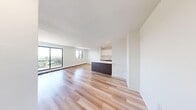 This 2-bedroom, 1-bathroom unit is thoughtfully laid out across a single floor, offering a functional and modern living environment. The open-concept kitchen and living room serves as the heart of the home, featuring light hardwood flooring that flows seamlessly throughout the entire unit. The kitchen is equipped with sleek, two-tone cabinetry — white upper cabinets paired with dark wood lower cabinets — and a large island with a white countertop that doubles as a breakfast bar. Stainless steel appliances, recessed lighting, and a clean, minimalist aesthetic complete the space. The generous living area is bathed in natural light from large sliding glass doors and windows that frame elevated views of the surrounding neighborhood and greenery beyond.

Both bedrooms are bright and well-sized, each featuring hardwood floors, windows with outdoor views, and baseboard heating. The primary bedroom includes a built-in sliding door closet for ample storage. A hallway connects the private areas of the unit. The full bathroom features a soaker tub with a tiled surround finished in crisp white subway tiles and chrome fixtures. Clean white walls and a neutral palette throughout lend the space a fresh, contemporary feel.