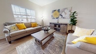 This two-story home is designed with a cohesive neutral palette of warm beiges and whites, creating a bright and welcoming atmosphere throughout. Hardwood-style flooring flows through the main living areas, adding warmth and continuity to the space.

The living room is a comfortable, well-lit area featuring large windows that invite natural light, angled ceilings that add architectural interest, and ample space for relaxed seating arrangements. Adjacent to it, the dining area is highlighted by sliding glass doors that open to an outdoor balcony, offering pleasant views of the surrounding neighborhood and filling the space with additional natural light.

The galley-style kitchen is efficiently laid out with rich dark cabinetry, stainless steel appliances, and generous counter space. A dedicated laundry room with a full-size washer and dryer adds everyday convenience.

A hallway with a staircase connects the floors, featuring clean white railings and recessed lighting. The bedrooms are carpeted for comfort, each with windows providing natural light. At least one bathroom features a dark wood vanity, a large mirror, and hardwood-style flooring, offering a clean and polished finish throughout.