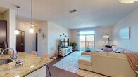 This single-floor residence offers a thoughtfully designed open-concept layout that seamlessly connects the kitchen, dining, and living areas. The living room is bright and welcoming, with a large sliding glass door leading to a private balcony that overlooks scenic outdoor views. The space is anchored by warm hardwood-style flooring and neutral walls that create a versatile, inviting atmosphere.

The kitchen is well-equipped for everyday living, featuring rich dark cabinetry, granite countertops, stainless steel appliances including a refrigerator and range, and ample storage on both sides of the galley-style layout. A breakfast bar provides a convenient transition into the open living space.

The bedroom is a serene retreat, finished with plush carpeting and natural light streaming through a generous window. The room offers ample space for furnishings and includes built-in storage options.

The bathroom is notably spacious, boasting an extended vanity with granite countertops, dark wood cabinetry, a wide mirror with overhead lighting, and a glass-enclosed shower. Light tile flooring and clean lines give the bathroom a polished, functional feel.

Overall, the residence combines practical design with modern finishes, offering a comfortable and cohesive living environment throughout its single level.