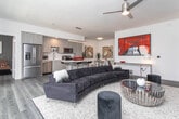 Unit 408 is a thoughtfully designed three-bedroom residence that blends contemporary aesthetics with functional living. The open-concept kitchen is a standout feature, outfitted with stainless steel appliances including a French door refrigerator, gas range, built-in microwave, and dishwasher. Flat-panel cabinetry in a light wood finish complements the clean white kitchen island, which provides additional seating and prep space. The adjoining dining area accommodates a round wood dining table, creating a seamless transition between cooking and entertaining spaces. The living room features hardwood-style flooring, a ceiling fan, and sliding glass door access, giving the space an open, airy feel. Each of the three bedrooms offers its own character — one with crisp white walls and a bright window, another with a bold accent wall and warm wood furnishings, and a third with neutral tones and ample natural light. The primary bathroom includes a dual-sink vanity with light wood cabinetry, white quartz countertops, a large mirror, and a glass-enclosed shower. A secondary bathroom features large-format tile flooring and a wall-mounted toilet, reflecting the same clean, modern design language carried throughout the entire residence.