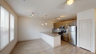 The Bay Front is a well-appointed 1-bedroom, 1-bathroom residence offering a thoughtfully designed single-level layout. The open-concept living and kitchen area creates a spacious, airy feel, with light wood-style flooring flowing seamlessly throughout the unit. Natural light fills the living area through large windows fitted with blinds, complemented by a ceiling fan overhead.

The kitchen is a standout feature, showcasing warm wood-tone cabinetry, granite countertops, and a light blue tile backsplash. A generous peninsula with an integrated sink and additional counter seating separates the kitchen from the living space. Stainless steel appliances — including a range, microwave, refrigerator, and dishwasher — complete the modern setup. Pendant lights and track lighting provide ample illumination throughout the kitchen.

The bedroom is a comfortable retreat with a ceiling fan and access to a spacious walk-in closet outfitted with wire shelving and wood-style flooring. The full bathroom features a soaking tub with large-format white tile surround, a wood-tone vanity with granite countertop, and coordinating wood-style flooring. Clean lines and neutral tones throughout create a cohesive, contemporary ambiance well-suited for modern living.