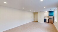 Located at 3500 Powelton Ave in the Powelton Village neighborhood of Philadelphia, PA, this thoughtfully designed unit offers a clean, modern aesthetic across a single floor. The open living area is finished with light-toned luxury vinyl plank flooring that runs throughout, contributing to a bright and cohesive feel. Recessed lighting is installed across the ceiling, providing even, adjustable illumination throughout the space. Natural light enters through multiple double-hung windows, enhancing the airy atmosphere of the main living area. A compact kitchenette is integrated into one end of the living space, featuring teal upper cabinetry, white lower cabinets, a stainless steel refrigerator, and a dishwasher — making efficient use of the available footprint. The entry area includes a closet with louvered doors, offering practical storage. The bathroom is well-appointed with a tub-shower combination accented by floor-to-ceiling vertical subway tile in a soft gray tone, a modern vanity with a warm wood cabinet and white countertop, a large mirror with black-framed detailing, and matte black fixtures throughout. Neutral tile flooring completes the bathroom's clean, contemporary look. The unit's crisp white walls and streamlined design create a functional and inviting living environment.