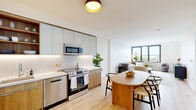 This well-appointed one-bedroom, one-bathroom residence at 280 Broadway in Bayonne, NJ offers a thoughtfully designed layout across a single floor. The open-concept living and kitchen area is anchored by large, dark-framed windows that flood the space with natural light and frame pleasant outdoor views. Light-toned hardwood flooring runs throughout, creating a cohesive and airy feel.

The kitchen is a standout feature, boasting a sophisticated blend of sage-toned upper cabinetry and warm wood lower cabinets, complemented by sleek white quartz countertops with under-cabinet lighting and a full suite of stainless steel appliances, including a french-door refrigerator, range, microwave, and dishwasher. Open shelving adds both function and style.

The living area is generously proportioned, with recessed lighting and expansive windows offering elevated views of the surrounding area. The bedroom is a serene retreat with ample closet space, natural light, and the same warm hardwood flooring.

The bathroom is elegantly finished with glossy vertical slate-blue wall tile, wood-look floor tile, a floating vanity with a wood base, and a clean, modern aesthetic throughout. This residence combines modern design with practical comfort in a well-located Bayonne address.