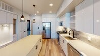 Located at 1680 E Gene Autry Way in Anaheim, California, this single-floor residence offers a clean, contemporary design throughout. The kitchen is a standout feature, outfitted with flat-front white cabinetry extending to the ceiling, stainless steel appliances including a gas range, microwave, dishwasher, and French door refrigerator. A central island with a light quartz countertop provides additional workspace, while pendant lighting and a tile backsplash add refined detail. Light wood-style flooring flows through the main living areas, enhancing the bright, open feel. The living space is generously proportioned and benefits from natural light through large windows, complemented by a ceiling fan. A built-in mudroom-style nook with shelving and storage cabinetry provides practical organization near the entry. The primary bathroom features a dual-sink vanity with white countertops and matte black fixtures, a soaking tub with subway tile surround, and direct access to a walk-in closet. A second bathroom includes a single vanity and additional storage. Bedrooms are well-sized, with plush carpeting, ceiling fans, and windows that invite natural light. The overall design aesthetic is modern and cohesive, combining neutral tones, matte black hardware, and durable finishes throughout.