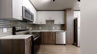 This single-floor unit presents a cohesive modern design throughout its thoughtfully arranged layout. The entry foyer opens via a solid white door with brushed nickel hardware, transitioning onto wood-look flooring that carries consistently through the living spaces, lending warmth and visual continuity.

The kitchen is a standout feature, designed with a two-tone cabinet scheme pairing crisp white upper cabinetry with rich wood-grain lower cabinets. A decorative linear tile backsplash in muted grey tones anchors the space between the cabinetry, while light quartz countertops provide a clean contrast. Stainless steel appliances, including a range, over-the-range microwave, and dishwasher, complete the fully equipped cooking space.

The living area is open and versatile, with bright white walls and recessed lighting creating a clean, neutral backdrop. A window allows natural light to enter, enhancing the airy feel of the room.

In-unit stacked laundry is conveniently integrated within the floor plan. The bathroom features floor-to-ceiling marble-look porcelain tile walls, wood-look tile flooring, a white quartz vanity top, and a wood-toned vanity cabinet, delivering a refined, spa-inspired aesthetic throughout.