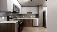 This single-floor unit presents a cohesive modern design throughout its thoughtfully arranged layout. The entry foyer opens via a solid white door with brushed nickel hardware, transitioning onto wood-look flooring that carries consistently through the living spaces, lending warmth and visual continuity.

The kitchen is a standout feature, designed with a two-tone cabinet scheme pairing crisp white upper cabinetry with rich wood-grain lower cabinets. A decorative linear tile backsplash in muted grey tones anchors the space between the cabinetry, while light quartz countertops provide a clean contrast. Stainless steel appliances, including a range, over-the-range microwave, and dishwasher, complete the fully equipped cooking space.

The living area is open and versatile, with bright white walls and recessed lighting creating a clean, neutral backdrop. A window allows natural light to enter, enhancing the airy feel of the room.

In-unit stacked laundry is conveniently integrated within the floor plan. The bathroom features floor-to-ceiling marble-look porcelain tile walls, wood-look tile flooring, a white quartz vanity top, and a wood-toned vanity cabinet, delivering a refined, spa-inspired aesthetic throughout.