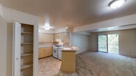 This single-floor residential unit offers a practical and functional layout designed for comfortable everyday living. The heart of the unit is an open-concept kitchen and living area, where the two spaces flow seamlessly into one another. The kitchen is well-appointed with light wood cabinetry offering ample storage, white appliances including a gas range with an overhead ventilation hood, and light-toned countertops that extend to a peninsula — ideal for casual dining or food preparation. Tile flooring in the kitchen transitions smoothly into the carpeted living area, which is generously proportioned and bathed in natural light from a large sliding glass door fitted with vertical blinds, providing access to outdoor views and greenery beyond. The bedroom is a quiet, well-sized room finished with plush carpeting and a window with blinds that allows natural light while maintaining privacy. The bathroom features a wide vanity with an integrated sink, substantial mirror, and wood-toned cabinetry below, complemented by a full tub and shower unit with clean white tile surround. Throughout the unit, neutral tones, flush-mount ceiling lighting, and clean lines create a calm, understated ambiance that is move-in ready and easy to personalize.