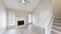 This single-floor residence offers a clean, modern aesthetic defined by a neutral warm palette, light-toned hardwood flooring, and an abundance of natural light streaming through slatted blinds. The living room serves as the centerpiece of the home, boasting dramatic vaulted ceilings that lend an impressive sense of openness and volume. A classic white wood-surround fireplace anchors the space, flanked by windows and a glass-paned exterior door that brings in natural light. A ceiling fan overhead adds both style and function to the airy room. The kitchen is well-appointed with stainless steel appliances, including a refrigerator, range, microwave, and dishwasher, complemented by white cabinetry, a grey subway tile backsplash, and granite-style countertops. The bedrooms are comfortable and well-sized, each equipped with ceiling fans and windows that allow natural light. One bedroom features a textured ceiling, adding subtle architectural contrast. The bathroom includes a tub-shower combination, white cabinetry with overhead storage, and a granite-style vanity countertop. Throughout the home, clean white trim, consistent flooring, and a cohesive neutral color scheme contribute to a bright, move-in-ready atmosphere.