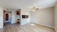 This single-story residence offers a practical and efficient layout across four bedrooms and two bathrooms. The combined living room and kitchen area serves as the heart of the home, featuring light wood-look flooring, neutral beige walls, and a textured ceiling with a ceiling fan and light fixture. A pass-through window with a countertop connects the kitchen to the living area, enhancing the open feel. The galley-style kitchen is equipped with warm wood cabinetry, a gas range, stainless steel refrigerator, tiled backsplash, and a double basin sink with ample counter space on both sides. Natural light filters into the living space through a front-facing window with blinds, and a solid wood entry door provides a welcoming entrance. Each bedroom continues the wood-look flooring and neutral palette, with ceiling fans, windows with blinds, and sliding closet doors for storage. The two bathrooms are functionally appointed: one features a walk-in tiled shower with a single vanity, while the second includes a full soaking tub/shower combo. A hallway and closet round out the floor plan, providing additional circulation and storage. The consistent finishes throughout create a cohesive, move-in-ready living environment.