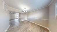 This single-story space is thoughtfully designed with consistent finishes throughout, creating a cohesive and well-maintained aesthetic. Wood-look flooring runs through the main living areas, complemented by neutral beige walls and crisp white trim and baseboards.

The dining area is a standout, featuring crown molding, a chair rail accent, and a brushed nickel chandelier with cylindrical shades that adds a refined touch. Natural light filters in through a window, brightening the open, airy feel of the space.

The living room continues the warm, neutral palette, with crown molding and a ceiling fan providing both style and comfort. A window allows additional natural light to enhance the room's welcoming atmosphere.

The galley-style kitchen is efficiently laid out with gray cabinetry, marble-look countertops, a stainless steel double sink, and black appliances, including a range and refrigerator. A window above the sink brings in natural light.

The bedroom offers generous storage with two separate closets and is fitted with a ceiling fan and a window. The full bathroom features a tiled tub-shower combination with a decorative mosaic accent border, a white vanity, and wood-look flooring.