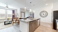 This single-floor residence is designed with a modern, open-concept layout that seamlessly connects the kitchen, dining, and living areas. The kitchen serves as a central focal point, anchored by a generous island with granite countertops, an integrated sink, and seating for casual dining. Gray shaker-style cabinetry pairs with stainless steel appliances and a subway tile backsplash, while cylindrical pendant lights hang above the island, adding a refined touch. Light wood-style flooring extends throughout the space, contributing to a bright and cohesive aesthetic.

The living area is well-lit by large windows that invite natural light and offer outdoor views, complemented by a ceiling fan and ample room for comfortable seating arrangements. A compact dining nook near the entrance provides an intimate space for meals or work.

Both bedrooms are generously proportioned, each featuring multiple windows that allow natural light to filter in, with light walls and the same wood-style flooring maintaining a consistent, airy feel. The full bathroom is finished with granite-topped blue-gray cabinetry, tile-surround tub and shower, and coordinating wood-look flooring, rounding out this well-appointed residence.