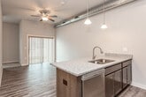 This well-appointed single-floor unit offers a thoughtfully designed open-concept layout that seamlessly connects the living and kitchen areas. The living space features durable wood-look plank flooring, neutral gray walls, and recessed lighting, creating a clean and versatile backdrop. Exposed ductwork running along the ceiling lends an industrial character to the space, complemented by a ceiling fan that enhances both style and airflow.

The kitchen is a standout feature, equipped with a full suite of stainless steel appliances including a refrigerator, range, and microwave. Rich dark cabinetry with granite-style countertops adds warmth and contrast, while a peninsula with pendant lighting provides a casual dining or prep space. The open sightlines between the kitchen and living area make the floor plan feel expansive and connected.

The bathroom is outfitted with modern brushed nickel fixtures, a tub and shower combination with a curved curtain rod, wood-look tile flooring, and a vanity topped with a light stone-look surface, delivering a clean and functional design.

Throughout the unit, consistent wood-look flooring, crisp white trim, and a neutral color palette contribute to a cohesive, contemporary aesthetic. The overall layout is efficient and well-organized, making excellent use of the available space.