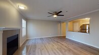 This single-floor unit is designed with a clean, contemporary aesthetic, featuring light hardwood-style flooring that extends consistently throughout the living areas, bedroom, and kitchen. The spacious living room serves as the focal point of the unit, anchored by a fireplace with a white mantle surround and flanked by windows fitted with blinds that allow for adjustable natural light. Crown molding lines the upper perimeter of the living area, adding a refined architectural detail, while a ceiling fan with integrated lighting provides both comfort and illumination. An arched passageway connects the living room to the kitchen, lending a classic design touch to the otherwise modern interior.

The kitchen is well-appointed with white shaker-style cabinetry, light gray countertops, a subtle tile backsplash, and a full suite of stainless steel appliances including a refrigerator, electric range, and over-the-range microwave. The bedroom is a comfortable, well-lit space featuring its own ceiling fan and a generously sized window with outdoor views. The bathroom includes a white vanity with a dark countertop, an undermount sink, and a tub-shower combination with clean white tile surround. Textured ceilings are present throughout, complementing the unit's understated, neutral color palette.