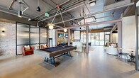 Located at 1015 Boulevard SE in Atlanta's Grant Park neighborhood, this single-floor amenity space blends industrial design with contemporary comfort. Soaring exposed ceilings reveal a network of ductwork and conduit overhead, complemented by polished concrete floors that flow throughout the expansive open layout.

The main lounge area is anchored by a curated mix of seating — including a soft pink sofa, rounded ivory armchairs, and colorful accent ottomans — arranged around a sculptural wood coffee table. Exposed brick walls and mounted flat-screen TVs add character and function. The space transitions seamlessly into a game area centered on a substantial billiards table beneath stylish pendant lighting.

A dedicated dining zone features a grand communal table, banquette seating, and elegant gold chandeliers, creating an upscale yet welcoming atmosphere. Floor-to-ceiling windows and glass doors along one wall flood the space with natural light and offer views of the outdoor pool area beyond.

A glass-enclosed private room with vibrant red-toned flooring and a crystal chandelier serves as a refined conference or meeting space. A well-appointed kitchenette with hexagonal tile flooring, open shelving, and stainless steel appliances supports event and gathering needs. Throughout, the design balances industrial rawness with warm, stylish furnishings.