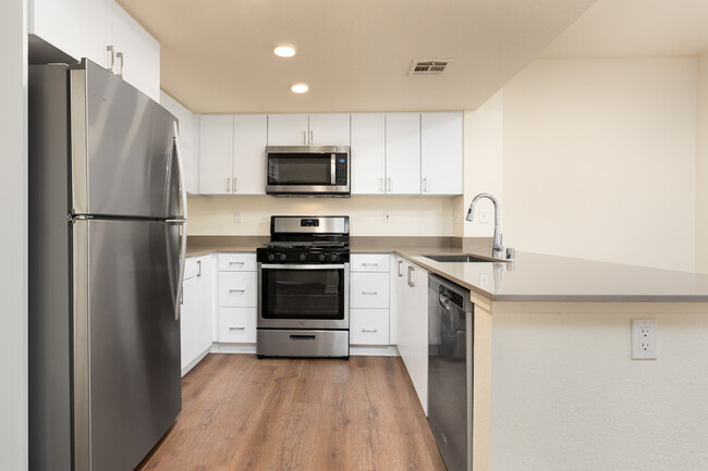 Renovated Package I kitchen with stainless steel appliances, grey quartz countertops, white flat cabinetry, and hard surface flooring - eaves Thousand Oaks