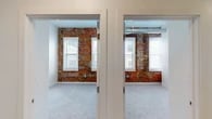 Located on Lorain Avenue in Cleveland's vibrant 44113 zip code, this single-floor unit masterfully combines historic industrial character with contemporary design. The space features striking exposed brick accent walls throughout, paired with crisp white walls and ceilings to create a warm yet modern aesthetic. Exposed ductwork adds to the industrial loft feel in several rooms.

The living and common areas are finished with light-toned hardwood flooring, recessed lighting, and generous ceiling height, giving the space an open and airy quality. Large windows with white blinds invite abundant natural light while framing views of the surrounding neighborhood.

The kitchen is a standout feature, showcasing sleek white upper cabinetry, warm wood-toned lower cabinets, stainless steel appliances, and a spacious white quartz waterfall island with an undermount sink and stylish pendant lighting overhead.

The bedrooms are carpeted for comfort and each benefit from the signature exposed brick walls and well-proportioned windows. The bathroom is finished to a high standard, featuring large-format wood-look tile in the walk-in shower, a wood-grain vanity with a white countertop, and light hardwood flooring, completing the cohesive blend of warmth and modern simplicity found throughout the space.