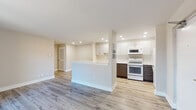 This thoughtfully renovated single-floor unit offers a bright, open layout finished with light hardwood-style flooring throughout the main living areas. The living room is spacious and airy, featuring neutral warm-toned walls, clean white baseboards, and a sliding glass door that brings in natural light and provides access to an outdoor space. A peninsula with a white countertop seamlessly connects the living area to the kitchen, creating an open and functional flow.

The kitchen is a standout feature, designed with a modern two-tone aesthetic combining crisp white upper cabinets and rich dark lower cabinets, all topped with bright white countertops. It is fully equipped with a gas range, over-the-range microwave, dishwasher, and refrigerator, all in white. Recessed lighting illuminates the workspace effectively, and a stainless steel sink adds a refined touch.

The bedroom is carpeted for comfort, featuring a window with blinds that allows natural light in, a wall-mounted air conditioning unit, a baseboard heater, and an open closet with hanging rod for convenient storage.

The bathroom is clean and functional, featuring a tiled tub-and-shower combo, a wall-mounted storage cabinet, towel bars, and baseboard heating. The overall unit presents a fresh, move-in-ready aesthetic throughout.