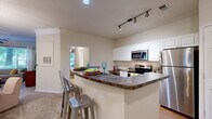 Located at The Bristol in Chesapeake, Virginia, this well-appointed 2-bedroom, 2-bathroom residence offers a thoughtfully designed single-level layout. The kitchen is a functional centerpiece, featuring white shaker cabinetry, dark granite countertops, stainless steel appliances including a refrigerator, electric range, and built-in microwave, plus a breakfast bar with seating — ideal for casual dining. Rich hardwood flooring grounds the kitchen area, while neutral carpet flows throughout the living spaces. The living room impresses with crown molding, a ceiling fan, and large windows that flood the room with natural light and offer lush outdoor views. A graceful arched doorway connects the living room to a sunlit sitting area, enhancing the open, airy feel of the space. Both bedrooms are comfortably sized, with the primary bedroom offering ample room and a dedicated closet. Each bathroom includes a granite-topped vanity with white cabinetry and a tub/shower combination with hardwood flooring. A hallway provides a smooth flow between all rooms. Throughout the residence, neutral tones, generous natural light, and quality finishes create a warm, inviting ambiance suited for everyday living.