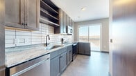 This efficiently designed single-floor unit offers a thoughtfully arranged layout encompassing two kitchens and two bathrooms within a compact footprint. The interior is finished with large-format tile flooring throughout, creating a cohesive and clean aesthetic that flows from room to room.

Each kitchen is outfitted with stainless steel appliances, including a range, microwave, and dishwasher. Dark-toned shaker-style cabinetry pairs with light granite countertops and a white subway tile backsplash, offering a modern contrast. Open upper shelving adds functional display space, while a matte black faucet at the undermount sink provides a refined accent. Large sliding glass doors in the kitchen area admit generous natural light and open to a balcony with an outdoor view.

A sliding barn door serves as a distinctive architectural detail, contributing both style and space efficiency along the main corridor. The hallway also features a recessed utility panel and track lighting overhead.

Both bathrooms are finished with tile flooring in a neutral palette. One bathroom includes a white soaking tub with white tile surround and matte black fixtures. Dark cabinetry with marble-style countertops adds consistency with the kitchen's design language. The textured wall surfaces throughout reinforce the unit's modern, structured aesthetic.