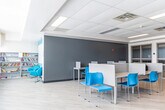 Located at 1700 Simcoe St N in Oshawa, Ontario, this single-floor open-concept workspace is thoughtfully designed to support focused study and collaborative activity. The room is finished with light wood-look luxury vinyl flooring that lends a clean, contemporary aesthetic throughout. A drop ceiling with recessed panel lighting ensures consistent, even illumination across the entire space.

Workstations are arranged in multiple configurations along the perimeter walls and in the open floor area, each equipped with individual privacy dividers in a warm cork-toned finish. Vibrant blue chairs provide a striking contrast against the neutral palette of white and grey walls, adding a lively, modern character to the environment.

One wall features large-format windows spanning nearly its full width, flooding the interior with abundant natural light and offering views of the surrounding outdoor landscape. Adjacent wall sections feature white square-tiled surfaces, contributing to the space's clean, institutional design.

A glass-paneled interior partition separates a secondary area at one end, providing a degree of visual division while maintaining an open feel. The layout is flexible and well-suited to individual study, group work, or shared workspace use, making it a highly functional and welcoming environment for its occupants.