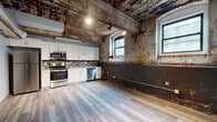 Located at 2000 E Westmoreland St in Philadelphia, PA, this single-floor space masterfully combines raw industrial heritage with contemporary updates. The open layout is anchored by strikingly weathered exposed brick walls and a richly textured ceiling with visible wooden beams and aged patina, lending the space an authentic, loft-like character. Light hardwood flooring runs throughout, providing a clean contrast to the rugged architectural elements above and around.

The kitchen is a standout feature, outfitted with crisp white cabinetry, granite countertops, and a full suite of stainless steel appliances including an electric range, microwave, and dishwasher. A mosaic tile backsplash adds visual interest, while arched windows with modern black frames invite natural light and frame views of the surrounding neighborhood.

Exposed HVAC ductwork and track lighting reinforce the industrial aesthetic in the living area, where a structural column bearing layers of aged paint serves as a unique design element. The space also includes a closet and direct access to a full bathroom.

The bathroom offers a clean, modern retreat finished in neutral tile flooring, a white vanity with granite countertop, and a full tub-shower combination clad in elegant marble-look subway tile. Together, these elements create a compelling blend of historic character and modern livability in the heart of Philadelphia.