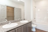 This single-floor unit showcases a thoughtfully designed open-concept layout that connects the living and kitchen areas seamlessly. The kitchen is outfitted with grey shaker-style cabinetry, speckled granite countertops, and a full suite of stainless steel appliances, including a refrigerator, electric range, and over-the-range microwave. A peninsula with pendant lighting serves as both a functional workspace and a casual dining option, with warm wood-look flooring tying the space together.

The living area features plush neutral carpeting, multiple windows that allow generous natural light, a sleek built-in electric fireplace, and a door providing direct outdoor access. The bedrooms continue the carpeted aesthetic and are equipped with ceiling fans and walk-in closets offering ample storage.

Both bathrooms are finished with grey vanity cabinetry, granite-style countertops, and full soaking tub and shower combinations. Wood-look flooring runs throughout both bathrooms, maintaining visual consistency with the rest of the unit. The overall design palette of neutral tones, modern fixtures, and consistent finishes creates a clean, contemporary ambiance throughout the space.