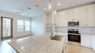 Located at 5701 Summerall Vista Circle in Riverview, FL, this thoughtfully designed one-bedroom, one-bathroom residence offers a bright and modern living experience across a single floor. The open-concept layout seamlessly connects the kitchen and living room, creating an efficient yet spacious flow throughout the home. Light hardwood-style flooring runs throughout, complementing the clean, neutral color palette.

The kitchen is a standout feature, anchored by a large granite-topped island with an undermount sink and elegant pendant lighting overhead. White shaker cabinetry extends to the ceiling, maximizing storage, while a subway tile backsplash and stainless steel appliances — including a refrigerator, range, and microwave — complete the polished look. Built-in shelving in the adjoining living area adds functional character.

The living room benefits from multiple windows and a glass door that opens to a balcony, flooding the space with natural light and offering views of the surrounding community. A ceiling fan adds comfort to this airy area.

The bedroom is a comfortable retreat with a large window framing outdoor views. It connects to a well-appointed bathroom featuring granite countertops, white cabinetry, and a glass-enclosed shower. A walk-in closet with wire shelving provides ample organized storage.