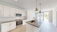 Located at 3612 Beverly Cove Way in Wilmington, NC, this thoughtfully designed one-bedroom, one-bathroom residence offers a clean, modern aesthetic highlighted by light wood-look flooring and crisp white trim throughout. The open-concept kitchen serves as the centerpiece of the home, featuring white shaker-style cabinetry, a classic subway tile backsplash, dark quartz countertops, and a full suite of stainless steel appliances including a refrigerator with ice maker, electric range, and built-in microwave. A central kitchen island with an undermount sink and bronze pendant lighting above adds both function and style, flowing seamlessly into the living area. French doors at the rear of the living space invite natural light and provide outdoor access. The bedroom is comfortably proportioned, outfitted with crown molding, a ceiling fan, and dual windows offering views of the surrounding community. A generously sized walk-in closet with wire shelving provides ample storage. The bathroom is finished with a white vanity with dark countertop, a tall linen cabinet, gold-toned fixtures, and wood-look flooring that ties the space together cohesively. Crown molding and recessed lighting are present throughout, lending a polished, refined character to this efficiently designed home.