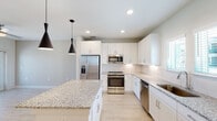 This well-designed 3-floor home offers a clean, contemporary aesthetic throughout, with light wood-tone flooring and neutral tones creating a bright and cohesive atmosphere across all levels. The ground floor includes a spacious attached garage with an automatic opener, providing convenient and secure parking.

The main living level showcases an open-concept layout where the kitchen flows seamlessly into the living area. The kitchen is a standout feature, outfitted with crisp white shaker cabinetry, granite countertops, a generous center island with pendant lighting overhead, and a full suite of stainless steel appliances including a range, microwave, dishwasher, and French door refrigerator. A door from the living area opens to an outdoor balcony, enhancing the sense of openness and allowing natural light to fill the space. A convenient half bath with a pedestal sink is also found on this level.

The upper floor hosts the bedrooms, each fitted with ceiling fans and multiple windows dressed with horizontal blinds that frame views of the surrounding neighborhood. The bathrooms are finished with granite-topped vanities, large framed mirrors, and light wood flooring. A dedicated laundry closet with full-size washer and dryer adds everyday practicality. The primary bathroom features a soaking tub and separate shower, completing this thoughtfully appointed home.