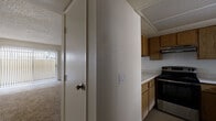This single-story residence features three bedrooms, two bathrooms, and a thoughtfully utilized floor plan that maximizes every square foot. The combined kitchen and living room serves as the central hub of the home. The kitchen is equipped with warm-toned wood cabinetry, a stainless steel range, a refrigerator, and light countertops laid out in an efficient L-shaped configuration with tile flooring. The adjacent living room is carpeted and features a sliding glass door dressed with vertical blinds, allowing natural light to filter in and providing outdoor access.

Each of the three bedrooms is finished with neutral-toned carpet and light walls, creating a clean and versatile space. The primary bedroom offers a comfortable footprint, while the secondary bedrooms are well-sized. At least one bedroom features a sliding-door closet with a built-in shelf and hanging rod, offering practical storage. Windows with vertical blinds are present throughout, providing light control.

The two bathrooms are each fitted with a full tub-shower combination, a toilet, and a wood-framed vanity with a sink. Textured ceilings are a consistent architectural detail found throughout the home. Two hallways connect the rooms, contributing to an organized and navigable interior layout.