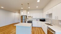 This well-designed one-bedroom, one-bathroom residence offers a thoughtfully planned single-floor layout with a clean, modern aesthetic. The open-concept living and kitchen area is bright and airy, featuring warm hardwood-style flooring, recessed lighting, and large windows that fill the space with natural light and offer views of the surrounding greenery.

The kitchen is a standout feature, showcasing crisp white cabinetry, a light gray subway tile backsplash, a white quartz center island with pendant lighting overhead, and a full suite of stainless steel appliances including a refrigerator, range, and dishwasher. Ample counter and cabinet space make this kitchen both functional and stylish.

The living area flows seamlessly from the kitchen, offering generous space for everyday living. The bedroom is well-proportioned, carpeted for comfort, and bathed in natural light from multiple large windows with a ceiling fan overhead. The full bathroom features hardwood-style flooring, a tub-shower combination, and clean, neutral finishes throughout.

A dedicated in-unit laundry room houses a full-size Whirlpool front-loading washer and dryer with wire shelving above for additional storage. The overall design is modern and cohesive, with a neutral color palette and quality finishes that create a fresh, move-in-ready environment.