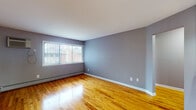 This single-floor space is characterized by consistent warm-toned hardwood flooring that extends throughout the living areas and bedrooms, complemented by cool lavender-gray painted walls and crisp white baseboards and ceilings. Multiple rooms benefit from natural light provided by windows fitted with vertical blinds, creating a bright and airy atmosphere. Baseboard heating units run along the exterior walls, ensuring efficient climate control, while at least one room also features a wall-mounted air conditioning unit. Ceiling fans with integrated light fixtures are present in select rooms. The layout, as visible in the floorplan view, includes several distinct rooms connected by doorways, offering a well-organized flow throughout the space.

The kitchen features warm oak cabinetry with ample storage, granite-look countertops, a stainless steel sink positioned beneath a large window, and stainless steel appliances including an electric range and over-the-range microwave. Tile flooring grounds the kitchen area. The bathroom includes a full tub-shower combination with floor-to-ceiling earth-toned ceramic tile surround, a natural light source from a window above the tub, and coordinating tile flooring, creating a cohesive and functional space.