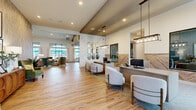 This single-story community clubhouse spans a generously sized footprint designed to serve multiple functions with a cohesive, contemporary aesthetic. The main entry opens into a welcoming leasing area featuring wood-look tile flooring, vaulted ceilings, and a staffed reception desk accented by a herringbone wood-panel backdrop. Decorative oval mirrors arranged in a grid pattern and pendant lighting add distinctive visual character to this zone, which includes comfortable upholstered seating for visitors.

Adjacent to the lobby, an open lounge area offers plush neutral seating, built-in shelving with a wall-mounted television, and large windows overlooking an outdoor pool area, filling the space with natural light. A full kitchenette features a wide quartz-topped island with bar seating, stainless steel appliances, lantern-style pendant lights, and an exposed brick accent wall.

A dedicated fitness center occupies a substantial portion of the floor plan, equipped with cardio machines, strength equipment, free weights, and rubberized flooring. A private office or flex room with carpeted flooring, built-in desk, and large windows completes the layout, providing a quiet workspace within the facility. Throughout, the design maintains a warm, neutral palette with quality finishes.