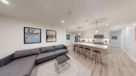 This thoughtfully designed single-floor space combines modern aesthetics with functional living. The open-concept layout seamlessly connects the living area and kitchen, creating a bright, airy atmosphere anchored by light wood-tone flooring and crisp white walls throughout.

The kitchen is a standout feature, equipped with a full suite of stainless steel appliances — including a French door refrigerator, electric range, built-in microwave, and dishwasher. Soft white shaker-style cabinetry lines the walls, complemented by a white subway tile backsplash and a generous white quartz island with bar seating for multiple guests. Two elegant globe pendant lights with brass accents hang above the island, adding warmth to the space.

The living area offers a comfortable sectional sofa, a glass-top coffee table, and wall-mounted artwork, alongside a dedicated media area with a wall-mounted flat-screen TV. Recessed lighting throughout ensures a well-lit environment.

The bedrooms are clean and minimalist, each featuring light wood flooring, modern black-framed windows, and ample closet space. The bathrooms are finished with white tile walk-in showers, dark-framed glass doors, and matte black fixtures, delivering a sleek, contemporary feel. The overall ambiance is modern, clean, and move-in ready.