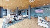 Located at 1143 Main St in Hartford, CT, this single-floor space offers a thoughtfully designed open-plan layout that seamlessly integrates a fully equipped kitchen with a spacious living area. The interior is defined by a striking combination of warm natural wood ceiling panels, light hardwood flooring, and textured blue-toned brick accent walls that lend the space a modern yet inviting character.

The kitchen is appointed with sleek dark countertops, light wood cabinetry, open shelving, a tile backsplash, and quality appliances. Stylish pendant lighting hangs above the counters, while floor-to-ceiling windows at the far end flood the workspace with natural light and provide views of the surrounding streetscape.

The living area is generously proportioned, anchored by a built-in fireplace set within a light masonry wall and framed by vertical wood paneling. Large windows along the perimeter invite abundant natural light throughout. Structural columns are integrated into the design, adding an industrial touch without disrupting the open flow. The lounge zone features multiple seating arrangements, with display screens mounted against the blue brick walls, making the space equally suited for relaxation or social gathering. The overall ambiance is warm, contemporary, and carefully curated.