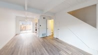 This well-appointed 2-bedroom, 1.5-bathroom residence spans two floors and offers a clean, modern aesthetic throughout. The main living level features light wood-style plank flooring that runs continuously through the open living area, which is highlighted by distinctive exposed ceiling beams painted white for a bright, airy feel. Large windows allow natural light to filter in, and sliding glass doors open to an outdoor area, enhancing the sense of openness. The kitchen is efficiently designed with stainless steel appliances including a refrigerator and range, a ventilation hood, white cabinetry, and a dedicated space for a stacked in-unit washer and dryer. A convenient half bathroom is also located on this level, featuring a compact corner sink, medicine cabinet mirror, and brushed nickel fixtures. Upstairs, both bedrooms continue the light flooring and crisp white walls, each equipped with a ceiling fan and roller shade window coverings. The primary bedroom includes a walk-in closet with sleek black-framed mirrored sliding doors. The full bathroom is thoughtfully finished with a tub-shower combination, white tile surround, a window for natural light, and a dark wood vanity with a white basin sink and brushed nickel hardware throughout.