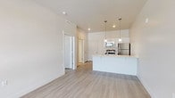 This single-floor residence features a contemporary, open-concept layout designed for functional everyday living. The main living area flows seamlessly into the kitchen, creating a connected and airy atmosphere. Light wood-style plank flooring extends throughout the common areas and bedroom, contributing to a cohesive and modern aesthetic.

The kitchen is well-appointed with a full suite of stainless steel appliances, including a refrigerator, electric range, over-the-range microwave, and dishwasher. White cabinetry with clean-lined hardware provides ample storage, while light-toned countertops offer generous prep space. A peninsula with pendant lighting above serves as both a functional workspace and a natural divider between the kitchen and living area. Recessed lighting supplements the pendant fixtures for well-distributed illumination.

The bedroom is a comfortably sized, quiet space with a window allowing natural light to enter. Its neutral walls and matching flooring maintain the consistent design language found throughout the unit.

The bathroom features a full tub-and-shower combination with a curved rod, a white vanity with storage below, and tile flooring in a warm neutral tone. Overall, the space presents a clean, move-in-ready environment with a consistently modern and understated design throughout.