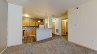 This single-floor unit offers a practical and comfortable layout centered around an open-concept living and kitchen area. The kitchen is well-equipped with warm honey-toned wood cabinetry — both upper and lower — providing ample storage, complemented by light laminate countertops and a gray tile backsplash. A white refrigerator and range anchor the cooking space, while pendant lighting and a track lighting system illuminate the area. A white breakfast bar peninsula separates the kitchen from the carpeted living area, creating a natural flow between the two spaces. The living area is spacious, with neutral-toned carpet and a textured ceiling, offering a comfortable setting for everyday use. A hallway leads to multiple bedrooms, each featuring plush gray carpet, neutral wall tones, and windows that bring in natural light with views of the surrounding building exterior. The unit includes two bathrooms: one featuring a full soaking tub with a shower/tub combo and wood-look vinyl flooring, and a second with a standalone walk-in shower stall, a wood-vanity with a sink, and a large mirror. Louvered closet doors add a classic touch throughout the private areas of the unit, while wood-look vinyl flooring ties together the wet areas and kitchen for easy maintenance.