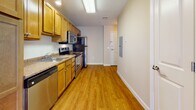 Located at 6 Timber Wood Dr in Lebanon, New Hampshire, this single-floor residence offers a functional and comfortable layout designed for everyday living. The kitchen is a standout feature, outfitted with warm honey-toned wood cabinetry, granite countertops, and a full suite of stainless steel appliances including a refrigerator, electric range, built-in microwave, and dishwasher. Hardwood-style flooring runs throughout the kitchen and entry area, adding a clean, durable finish to the space. An electrical panel is conveniently accessible near the entry. The open living and dining area is generously proportioned, with soft wall-to-wall carpeting underfoot and warm neutral-toned walls that create an inviting atmosphere. A pendant chandelier marks the dining space, while the living area benefits from multiple windows and sliding glass doors that flood the room with natural light and provide direct access to an outdoor patio with views of the surrounding landscape. The bathroom is thoughtfully laid out, featuring a walk-in shower with a curtain rod, a toilet, and tile flooring, all finished in neutral tones. Clean white trim and paneled doors are consistent throughout the unit, lending a cohesive and well-maintained aesthetic to the entire space.