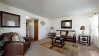 Located at 7627 E 37th St N in Wichita, Kansas, this single-floor home offers a thoughtfully designed layout with comfortable living spaces and warm, consistent finishes throughout. The living room serves as a welcoming focal point, featuring plush carpeting, neutral walls, and a wood-mantled fireplace framed by two windows that fill the room with natural light — ideal for relaxed everyday living. A second sitting area provides additional lounge space with easy access to the entryway and interior rooms. The dining area flows seamlessly into the kitchen through an open pass-through design, creating a connected and functional space. The dining room benefits from a ceiling fan and large windows dressed with curtains, allowing for ample natural light. The adjacent kitchen features warm wood cabinetry, a skylight, and white appliances, offering a practical and efficient workspace. The bedroom is carpeted and well-lit with multiple windows, providing a quiet and restful retreat. The bathroom is clean and functional, featuring wood-toned cabinetry with generous counter space, a mirrored medicine cabinet, and a full tub-shower combination. Hardwood flooring accents the bathroom and kitchen areas, complementing the home's warm, cohesive aesthetic throughout.