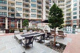 Located in the sought-after River Oaks area of Houston, Texas, this sophisticated outdoor amenity courtyard is a standout feature of the residential community at 2303 Mid Ln. The space is framed by multi-story buildings clad in a refined combination of brick and stucco, with balconies overlooking the courtyard at every level, creating a sense of enclosure and privacy without sacrificing openness.

At the heart of the space is a generously sized resort-style swimming pool with striking turquoise water, complemented by a separate spa with tiled steps. The pool deck is finished in a combination of herringbone-patterned brick and large-format stone pavers, lending a classic yet upscale aesthetic throughout. Sun loungers and shaded umbrella seating are thoughtfully arranged along the pool's edge for relaxation.

A dedicated fire pit lounge area features cushioned armchairs arranged around a central stone fire table, providing an inviting gathering spot. A covered outdoor kitchen and grilling station with adjacent dining seating adds to the entertainment appeal. Mature trees, sculptural planters, trimmed hedges, and ornamental grasses are woven throughout, softening the hardscape and adding vibrant greenery. Columned pergola structures and classic lantern-style lighting complete the refined, resort-inspired ambiance of this exceptional outdoor space.