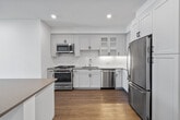 Located at 1650 S Delaware St, Unit 206 in San Mateo, CA, this thoughtfully designed single-floor residence offers a clean, contemporary aesthetic throughout. The open-concept kitchen is a standout feature, showcasing white shaker-style cabinetry with glass-front upper panels, a classic subway tile backsplash, stainless steel appliances including a range, microwave, dishwasher, and refrigerator, and a central island with a contrasting countertop — all set atop warm wood-tone flooring. The living area extends naturally from the kitchen and is bathed in natural light through large windows and a glass door that opens to an outdoor space with views of surrounding greenery. The bedrooms are carpeted for comfort and feature ceiling fans, natural light from well-placed windows, and a clean, neutral palette. The primary bathroom is generously proportioned, offering a walk-in shower with glass enclosure, a floating vanity with white quartz countertop and black hardware, and access to a walk-in closet with built-in shelving. A secondary full bathroom mirrors this refined aesthetic with a shower-tub combination and matching vanity finishes. Throughout the residence, crisp white walls, recessed lighting, and consistent wood-tone flooring create a cohesive and modern living environment.