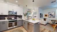 Located at 500 W Camelback Rd in Phoenix, Arizona, this well-appointed 2-bedroom, 3-bathroom residence offers a thoughtfully designed single-floor layout with modern finishes throughout. The open-concept kitchen and living area serves as the heart of the home, featuring a central island with white quartz countertops, two-tone cabinetry with white upper cabinets and gray lower cabinets, a dark tile backsplash, and stainless steel appliances including a gas range and side-by-side refrigerator. Pendant lighting illuminates the island, while light wood-tone flooring extends seamlessly into the bright living room, which benefits from natural light through French-style doors with plantation shutters. The two bedrooms offer a calm, neutral aesthetic with plush carpeting and curated wall art. The primary bedroom provides a comfortable retreat with dedicated nightstands and soft lighting. The bathrooms are finished with gray vanity cabinetry, white quartz countertops, illuminated mirrors, and glass-enclosed walk-in showers with clean white tile surround and chrome fixtures. The overall design balances contemporary style with functional living in a compact yet efficient floor plan ideal for urban Phoenix living.