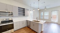 Located in Fort Worth, Texas, this well-designed single-story, one-bedroom, one-bathroom home offers a clean, modern aesthetic throughout. Warm hardwood-style flooring flows seamlessly across every room, complemented by crisp white walls and an abundance of natural light streaming through multiple windows fitted with horizontal blinds.

The combined kitchen and living area serves as the heart of the home. The kitchen is outfitted with sleek gray shaker-style cabinetry, stainless steel appliances including a side-by-side refrigerator with water and ice dispenser, an electric range, over-the-range microwave, and dishwasher, all set against a bright white backsplash.

The bedroom is a comfortable, light-filled retreat with windows overlooking the outdoors, providing a calm and airy atmosphere. A dedicated walk-in closet off the bedroom offers generous built-in shelving and hanging rods on multiple walls, maximizing storage efficiency.

The bathroom features a glass-enclosed walk-in shower adorned with elegant marble-look tile, gray cabinetry, and direct access to the walk-in closet, creating a practical and cohesive private suite. A glass door in the living area leads to an outdoor space, further enhancing the home's connection to the outside.