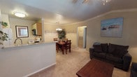 This single-floor, 1-bedroom, 1-bathroom unit is thoughtfully designed to maximize comfort and functionality. The open-concept living and dining area serves as the heart of the home, with plush carpeting underfoot and crown molding accenting the ceilings throughout. The living room offers ample space for seating, a ceiling fan with light fixture, and a large window fitted with blinds and sheer curtains that allow natural light to filter in. Adjacent to the living area, the dining space is defined by a chandelier overhead and provides a welcoming area for meals, flowing seamlessly into the kitchen. The kitchen features light wood cabinetry, tile-look countertops, and essential appliances including a range and microwave, with a breakfast bar separating it from the dining area. The bedroom is a serene retreat, complete with a ceiling fan, a generous window with sheer drapery that brings in soft natural light, and a walk-in closet. The full bathroom is well-equipped with a wide vanity featuring a speckled countertop and large mirror, tile flooring, and a shower-tub combination. Crown molding and neutral warm tones create a cohesive, inviting ambiance throughout the entire unit.