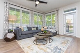 This single-floor residence at Bolton Drive NW in Atlanta, Georgia, offers a thoughtfully designed open-concept layout that seamlessly connects the main living areas. The living room is a bright, welcoming space anchored by an expansive bank of windows dressed with white plantation shutters and patterned drape panels, allowing generous natural light to filter in while framing views of surrounding greenery. Warm wood-look flooring runs throughout the main areas, lending a cohesive, modern aesthetic.

The kitchen is well-equipped and designed for both function and style. White upper cabinetry pairs with natural wood-toned lower cabinets and sleek quartz countertops. A spacious island with bar seating serves as a central gathering point, illuminated overhead by two matte black pendant lights. Stainless steel appliances, including a refrigerator, microwave, and range, complete the space alongside a subway tile backsplash.

The bedroom provides a comfortable retreat with plush carpeting, a ceiling fan, and access to both a walk-in closet with built-in rod storage and a private ensuite bathroom. The overall ambiance of the unit is contemporary and cohesive, with neutral tones, modern fixtures, and thoughtful design details throughout.