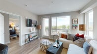 This single-floor residence offers a thoughtfully designed open-concept layout where the kitchen flows seamlessly into the living and dining areas. The kitchen is outfitted with stainless steel appliances, including a gas range, built-in microwave, and full-size refrigerator. Two-toned cabinetry pairs warm wood-finish uppers with crisp white lower cabinets, complemented by a chevron-patterned tile backsplash and light stone countertops. Wood-style flooring runs throughout the unit, lending a cohesive, contemporary feel.

The living room is a bright, airy space anchored by large sliding glass doors that open to a private balcony, offering expansive outdoor views and abundant natural light. A wall-mounted television and generous seating area make it an inviting gathering space. A versatile secondary room with a ceiling fan and large window serves well as a home office or additional bedroom.

The bedroom features a large window with scenic views, providing excellent natural light. Two well-appointed bathrooms include warm wood vanities, neutral countertops, and wood-style flooring. One bathroom offers a full soaking tub and shower combination, while the other provides a refined vanity with a large mirror, making both functional and polished.