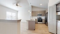 This single-floor residence offers a thoughtfully designed open-concept layout that seamlessly connects the living and kitchen areas. The kitchen is a standout feature, showcasing taupe shaker-style cabinetry that reaches toward the vaulted ceilings, a large peninsula with a light quartz countertop and undermount stainless steel sink, and a full suite of stainless steel appliances including a range, microwave, and refrigerator. Stylish pendant lights hang above the peninsula, adding a modern touch, while recessed lighting and a ceiling fan complete the space. Light-toned hardwood flooring flows throughout the main living areas, contributing to a bright and airy atmosphere enhanced by an abundance of natural light through multiple windows. The bedrooms are carpeted and generously sized, each featuring ceiling fans and multiple windows that bring in ample sunlight. The primary bedroom connects to a walk-in closet outfitted with wire shelving on multiple walls, offering excellent storage capacity. The bathroom is finished with large-format tile surrounding a soaking tub with a showerhead, complemented by hardwood-style flooring. A dedicated laundry closet with cabinetry is also present, adding everyday practicality to this well-appointed residence.